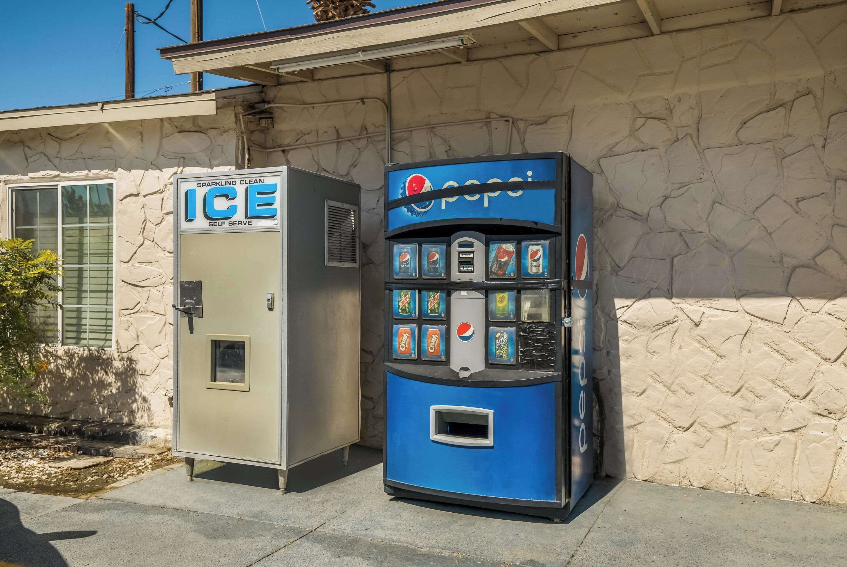 A vending machine with a Pepsi logo and a Sparkling Clean ice vending machine next to a building.