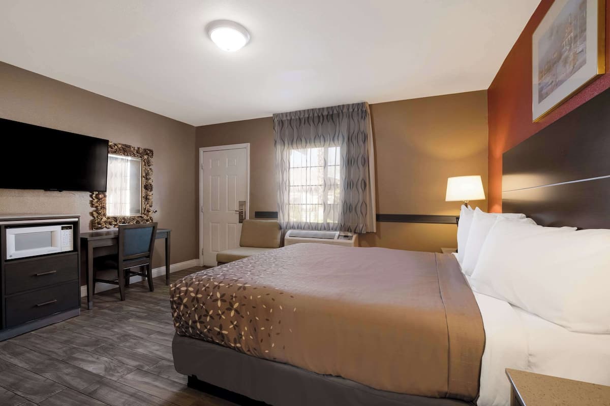 A hotel room with a bed, a desk, a chair, a television, and a window with curtains.
