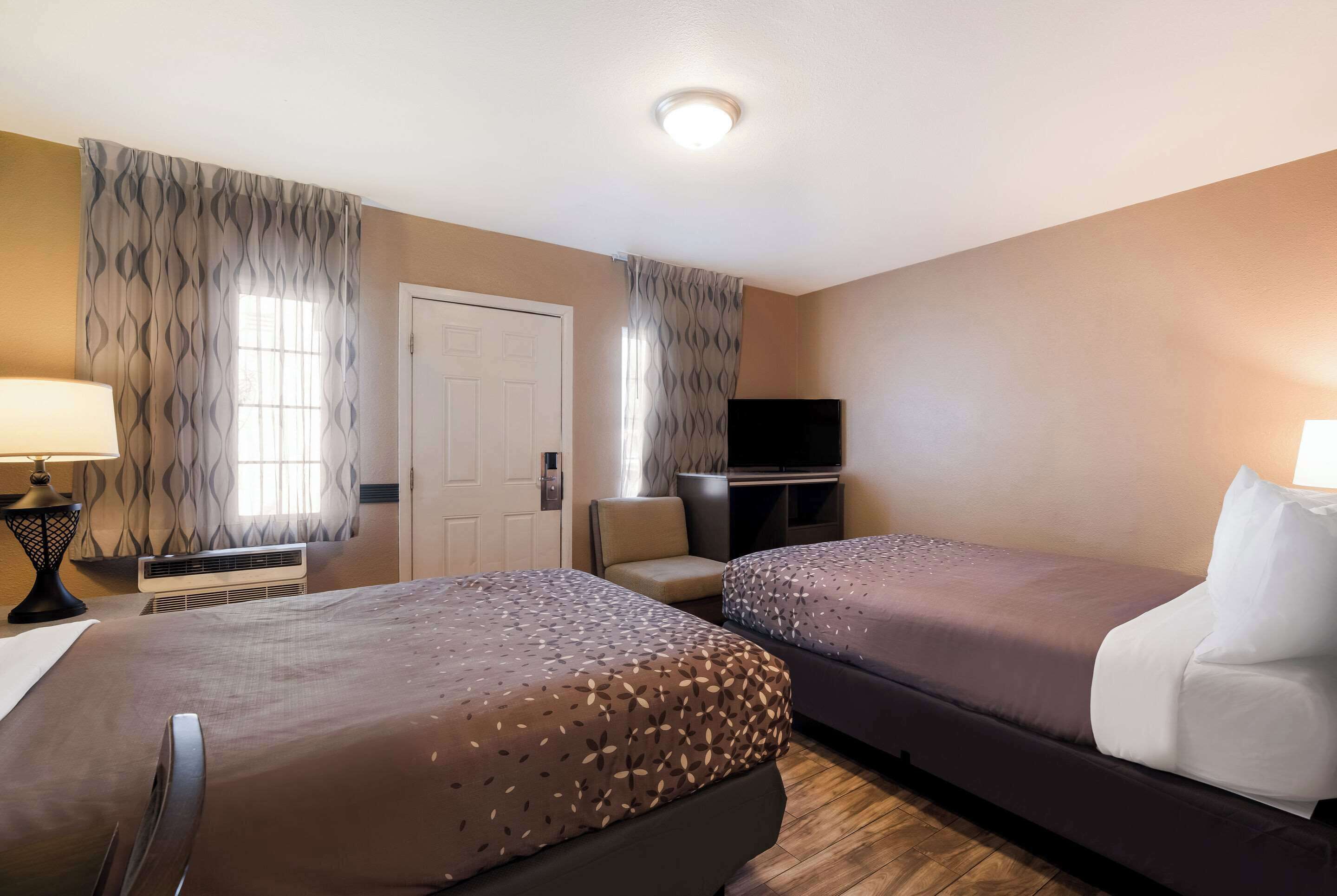 Een hotelkamer met twee bedden, een televisie, een stoel en een lamp.
