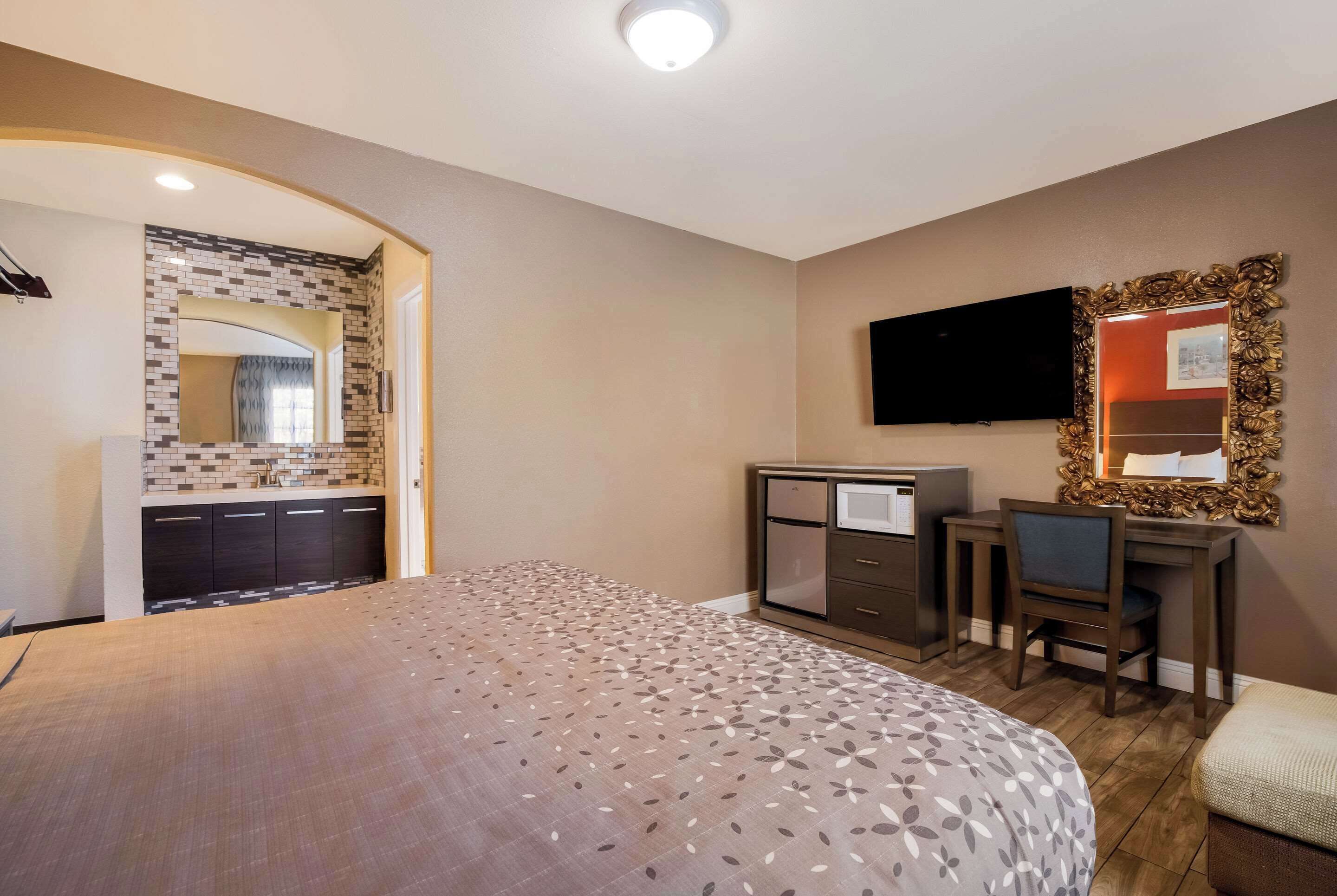 Un dormitorio con cama, escritorio, silla, televisor y baño con zona de ducha azulejada.