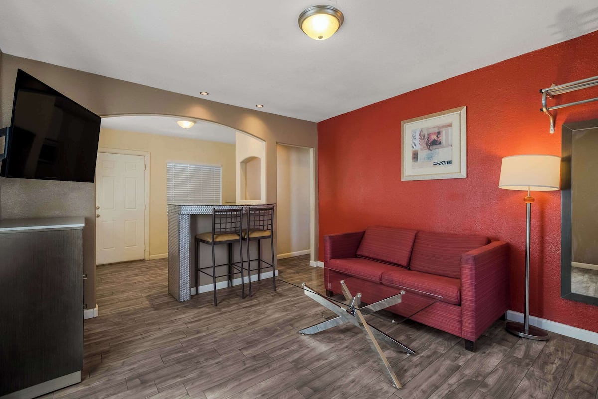 A compact living space with a kitchenette, a red sofa, a dining area with a bar stool, and a floor lamp.