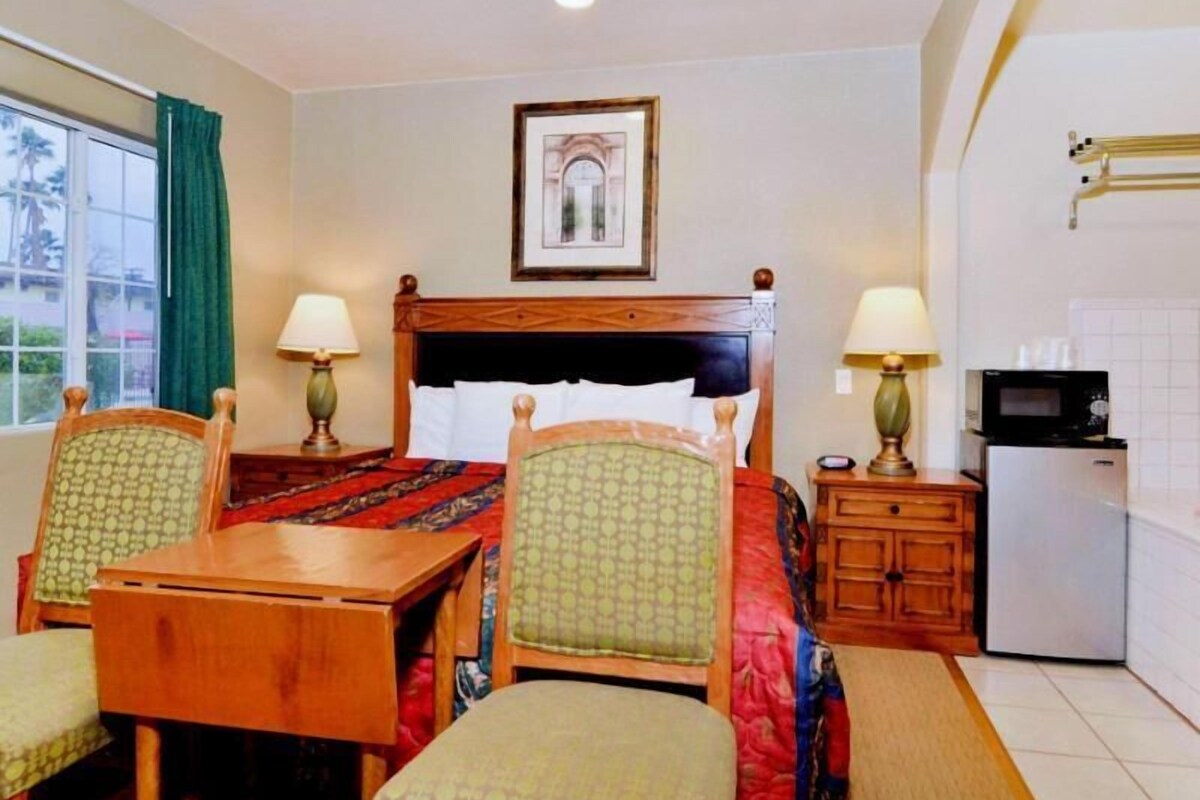 Ein Hotelzimmer mit einem Bett, einem Schreibtisch mit Stühlen, einer kleinen Küchenzeile und einem gerahmten Bild an der Wand.