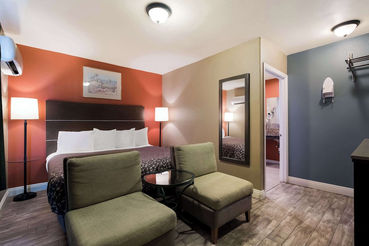 A hotel room with a bed, two chairs, a small table, a mirror, and a nightstand.