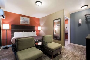 A hotel room with a bed, two chairs, a small table, a mirror, and a nightstand.