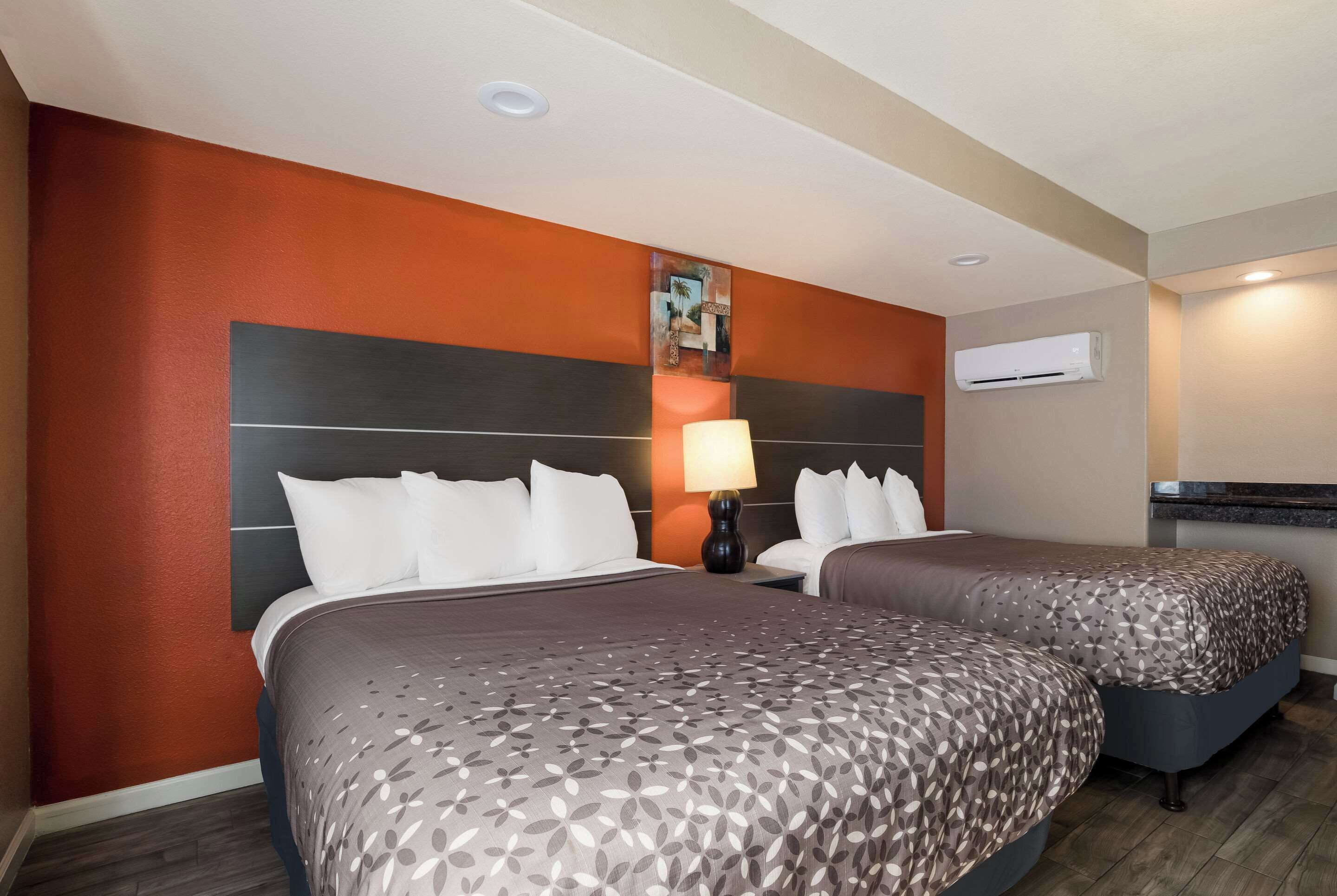 Camera d'albergo con due letti, un comodino, una lampada, condizionatore d'aria a muro e un angolo cottura.