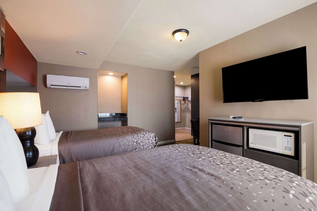 A hotel room with two beds, a TV, a microwave, and an air conditioning unit.