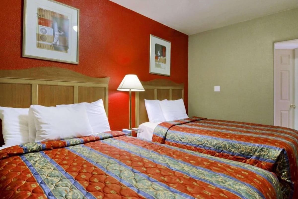 Ein Hotelzimmer mit zwei Betten, einem Holzkopfteil, einer Lampe und zwei gerahmten Bildern an der Wand.