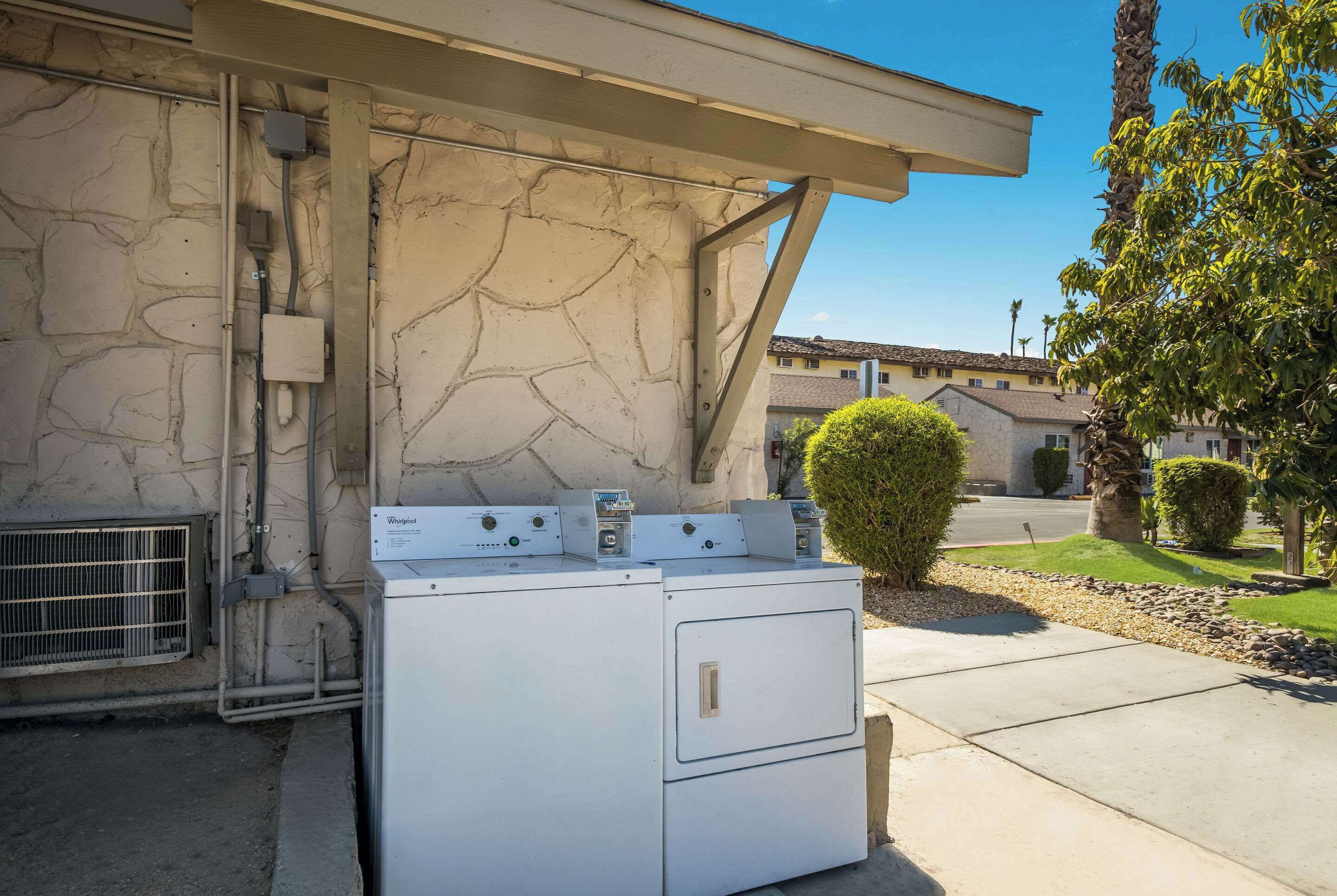 A laundry area with stacked washers and dryers, a stone wall, and a clear sky.