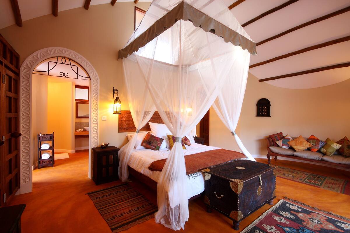 Un dormitorio con una cama con dosel, un cofre de madera y una alfombra estampada.