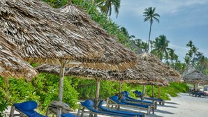 A beach with thatched umbrellas and wooden lounge chairs. - Kena Beach Hotel (Matemwe)