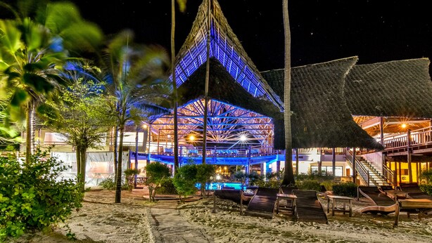 A beachside resort with a large building featuring a thatched roof and illuminated blue lights. - Kena Beach Hotel (Matemwe)