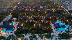 Vista aérea de un resort con varias construcciones tipo bungalow, una piscina central y acceso a la playa.
