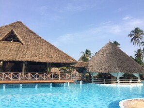 Un espace piscine agrémenté de structures à toits de chaume et d’une terrasse en bois.