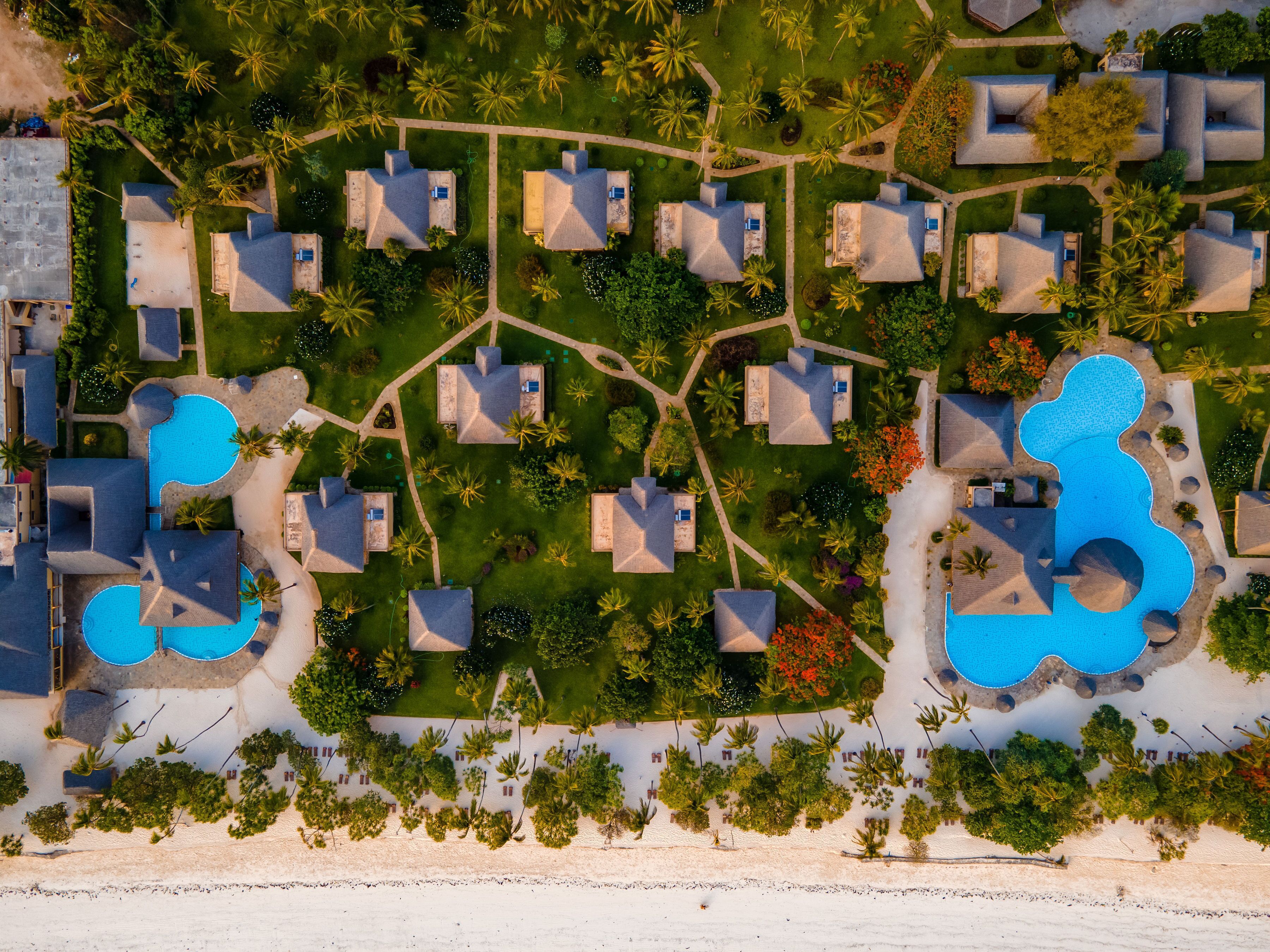 Eine Vogelperspektive zeigt ein Resort mit mehreren Bungalows, einem zentral gelegenen Pool und direktem Zugang zum Strand.