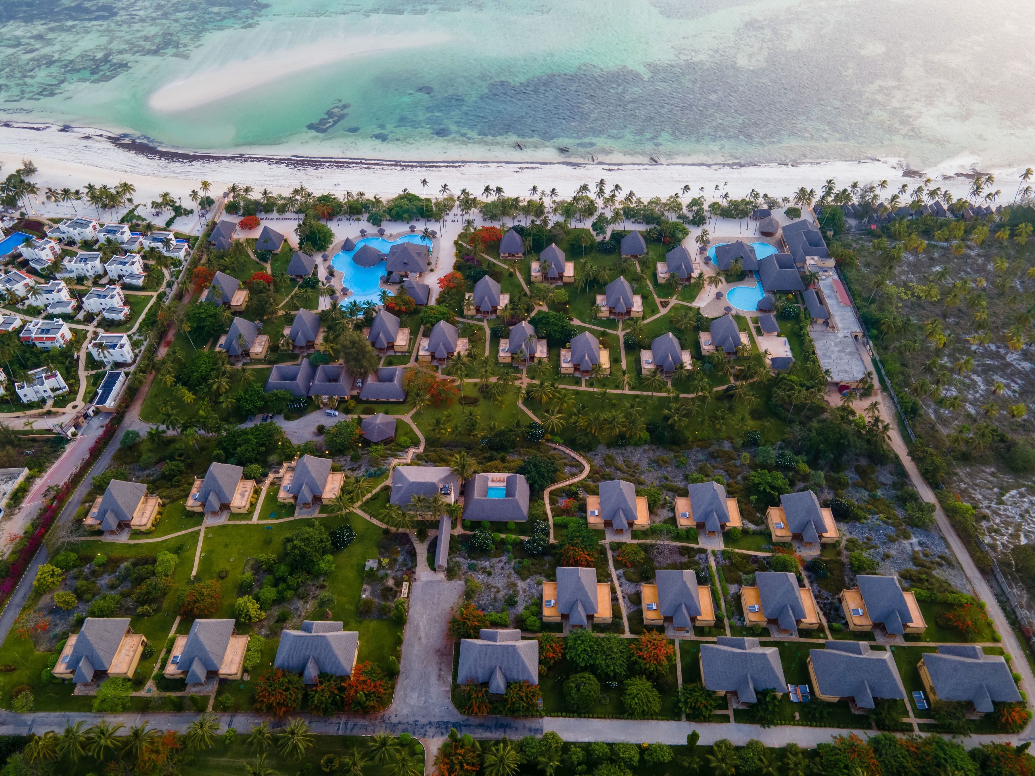 Vista aérea de un complejo turístico con varias cabañas, un área de piscina central y una playa junto a la propiedad.