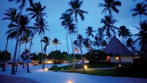 Un resort con palmeras, un edificio de techo de paja y una zona de playa.