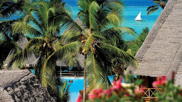 Un resort tropical con piscina, palmeras y vista al océano.