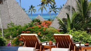 Un resort tropical con cabañas de techo de paja, palmeras y una zona de piscina con sillones de descanso.