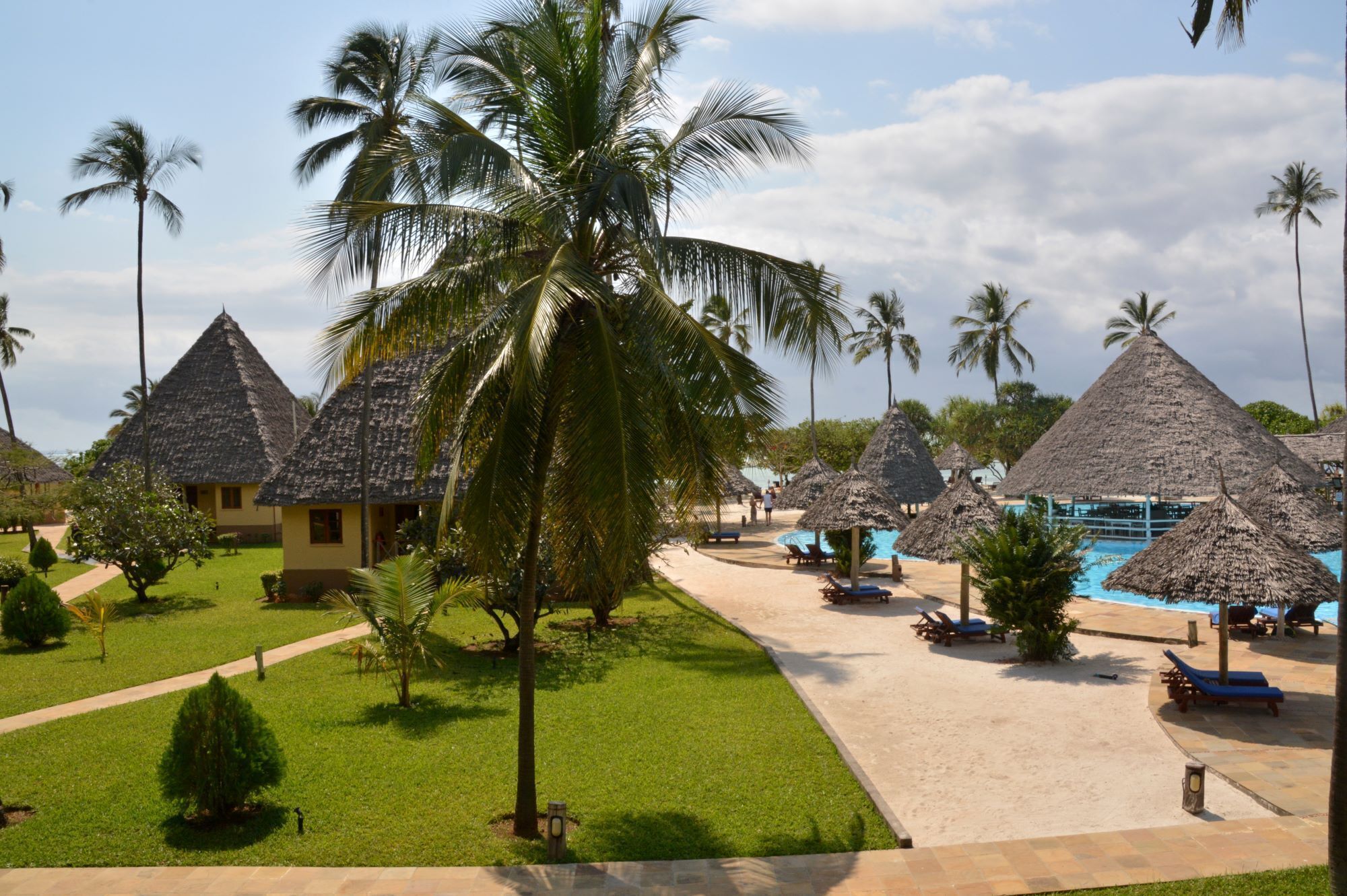 Un complexe hôtelier doté de bungalows aux toits de chaume, d’une piscine et d’une pelouse bien entretenue.