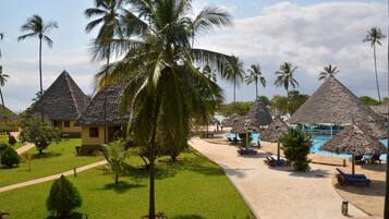 Un complexe hôtelier doté de bungalows aux toits de chaume, d’une piscine et d’une pelouse bien entretenue.