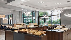A modern hotel breakfast area with a variety of food options, including pastries and breakfast items, and a view of the outdoors through large windows. - Residence Inn by Marriott Munich City East (Munich)
