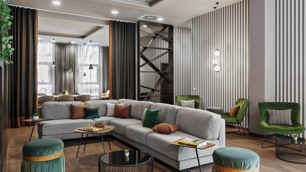 A modern living room with a sectional sofa, two ottomans, a coffee table, and a green armchair. - Residence Inn by Marriott Munich City East (Munich)