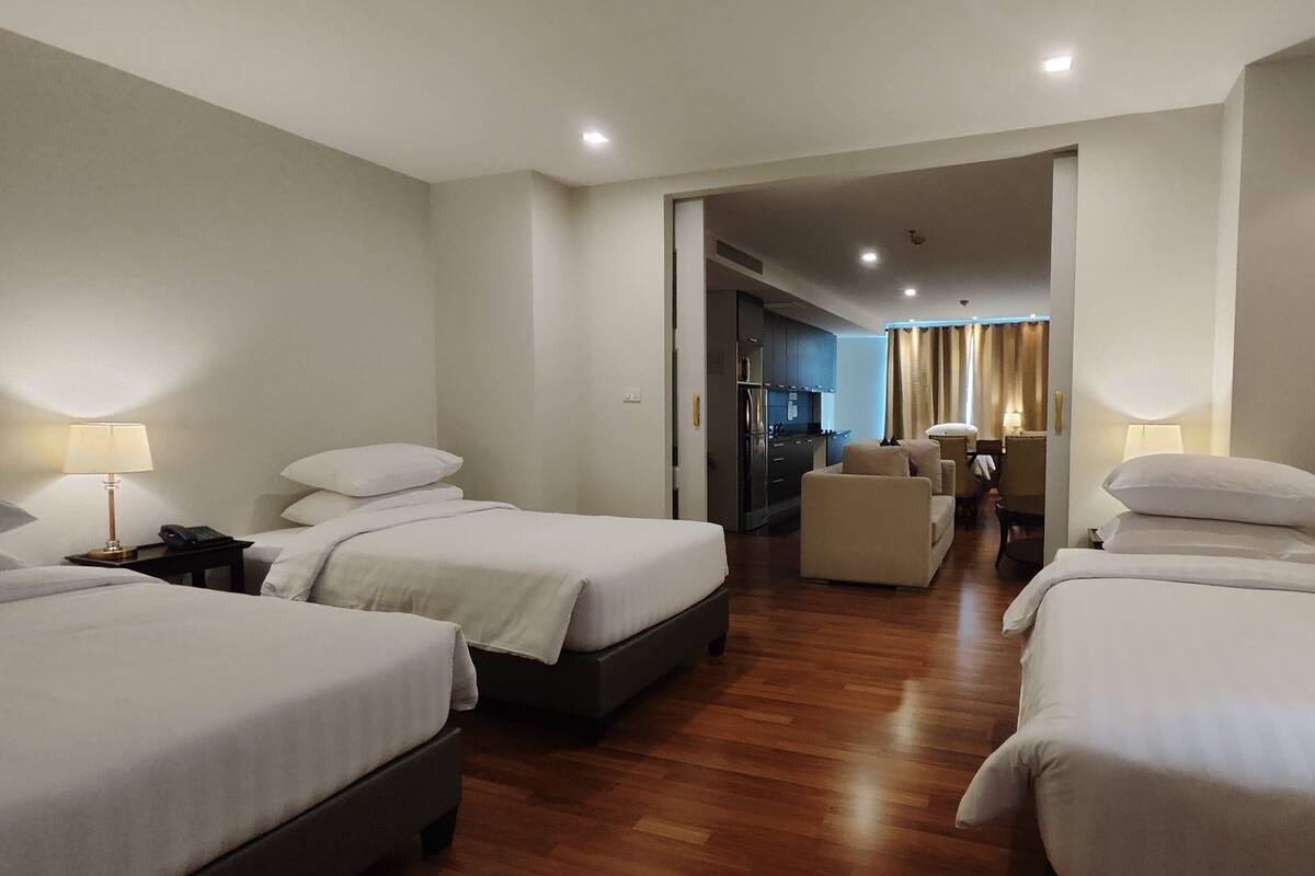 A hotel room with two beds, a desk, a chair, and a kitchenette.