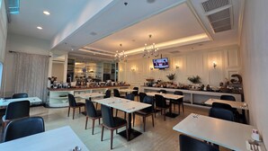 A modern restaurant with multiple dining tables and chairs, a kitchen area in the background, and a TV mounted on the wall. - The Bless Hotel and Residence (Bangkok)