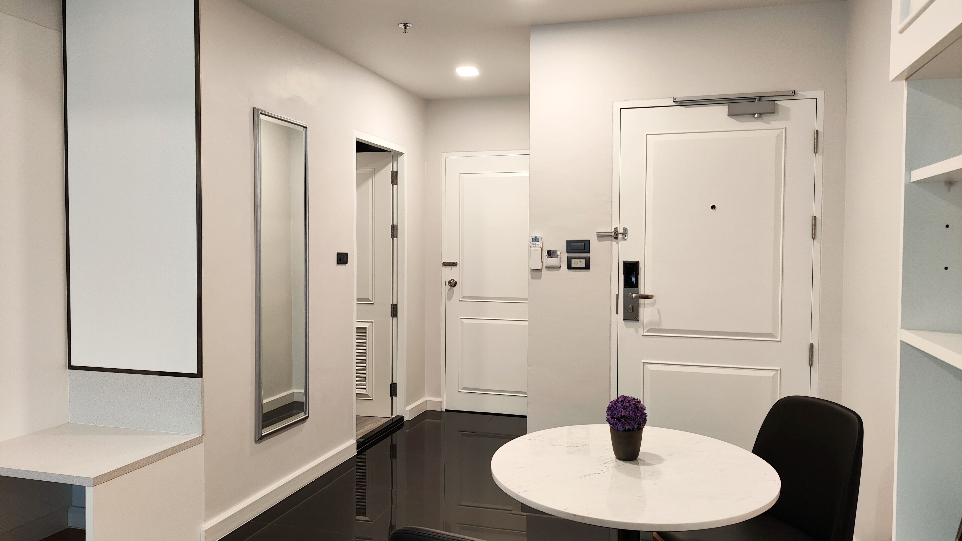A modern hotel hallway with a round table and chairs, a potted plant, and a mirror on the wall.