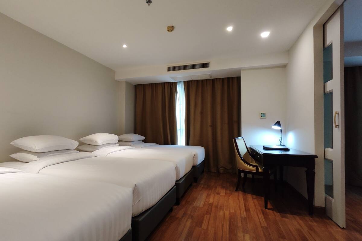 A hotel room with three beds, a desk with a chair, and a window with curtains.