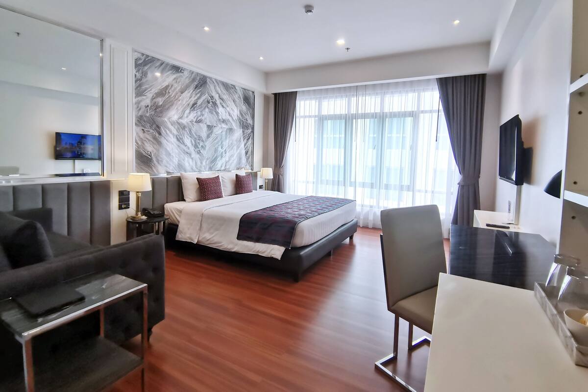 A modern hotel room with a large bed, a sofa, a desk, and a TV.