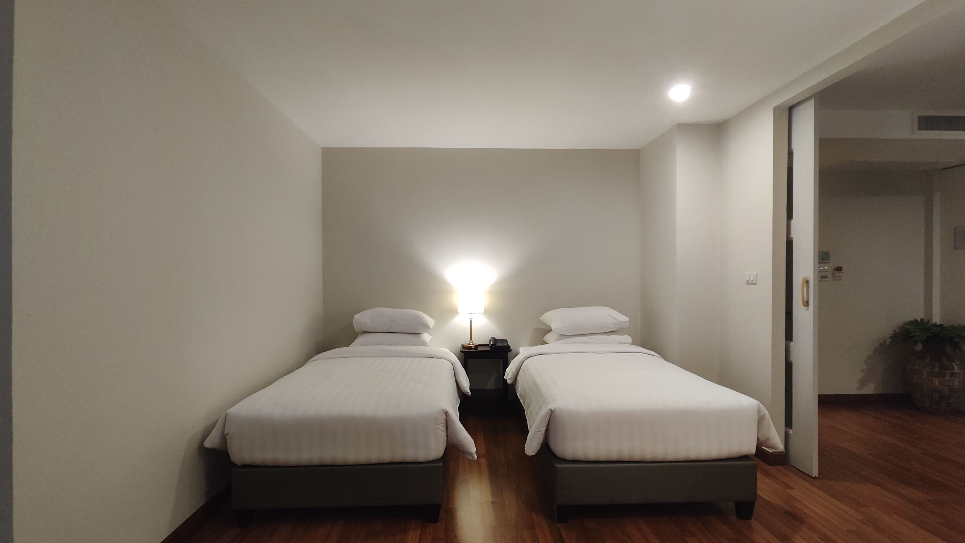 A room with two single beds, a bedside table with a lamp, and a wooden floor.