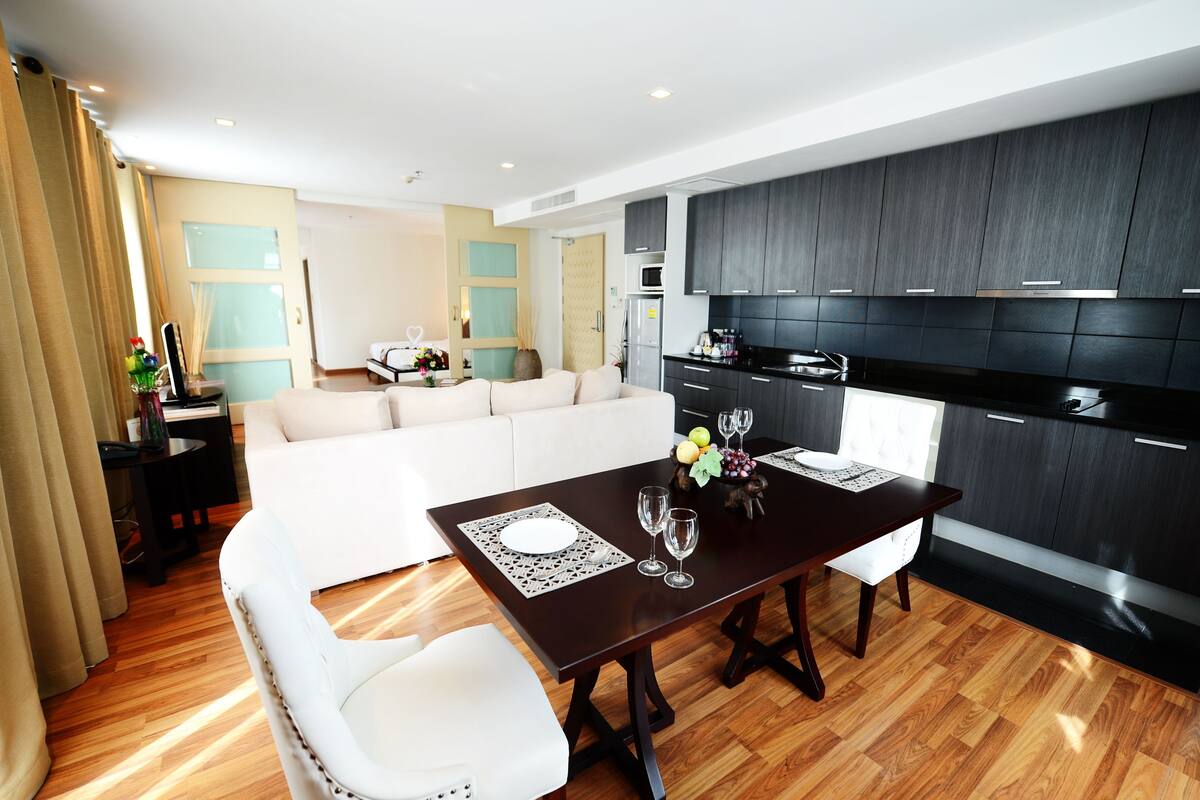 A modern living room with a dining table, white sofa, and dark kitchen cabinetry.