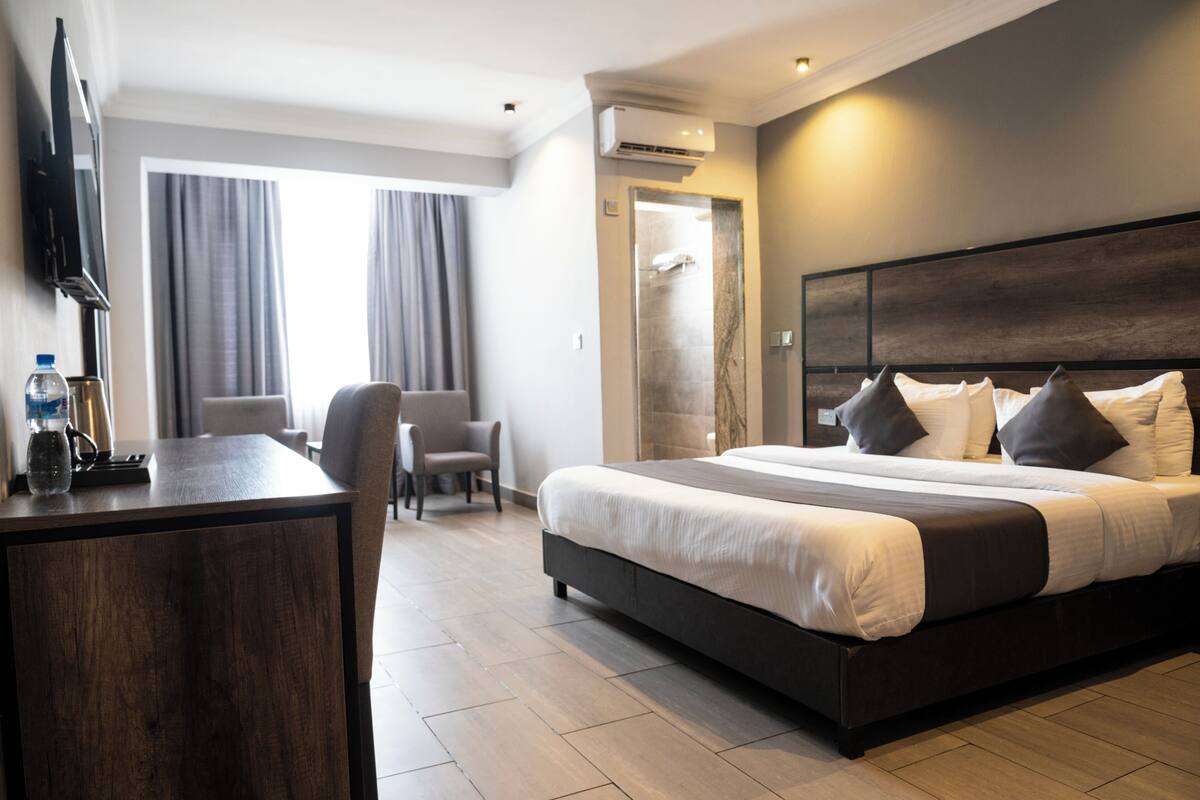 A modern hotel room with a large bed, a desk with a chair, a TV, and a shower area.