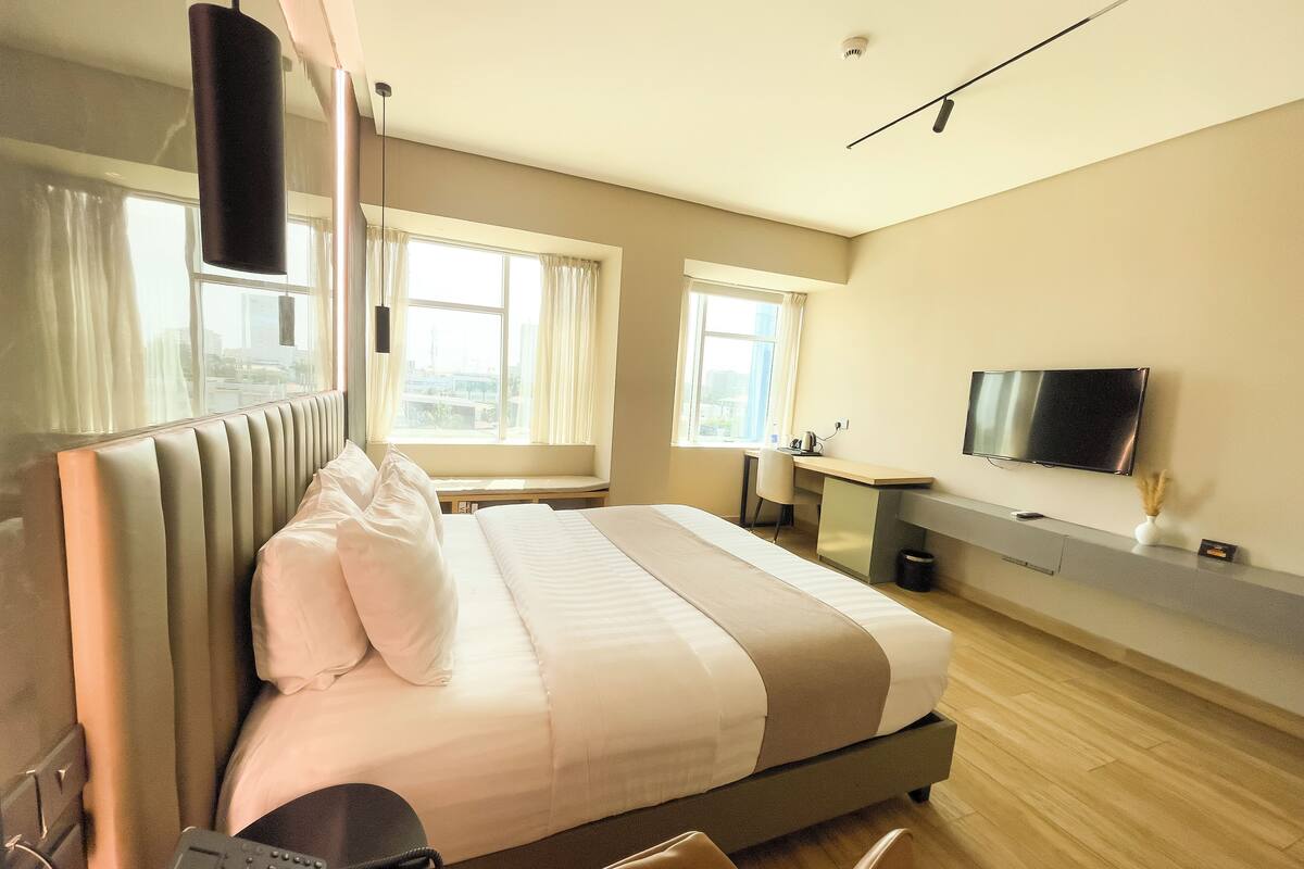 A hotel room with a bed, bedside table, chair, desk, TV, and a window with curtains.