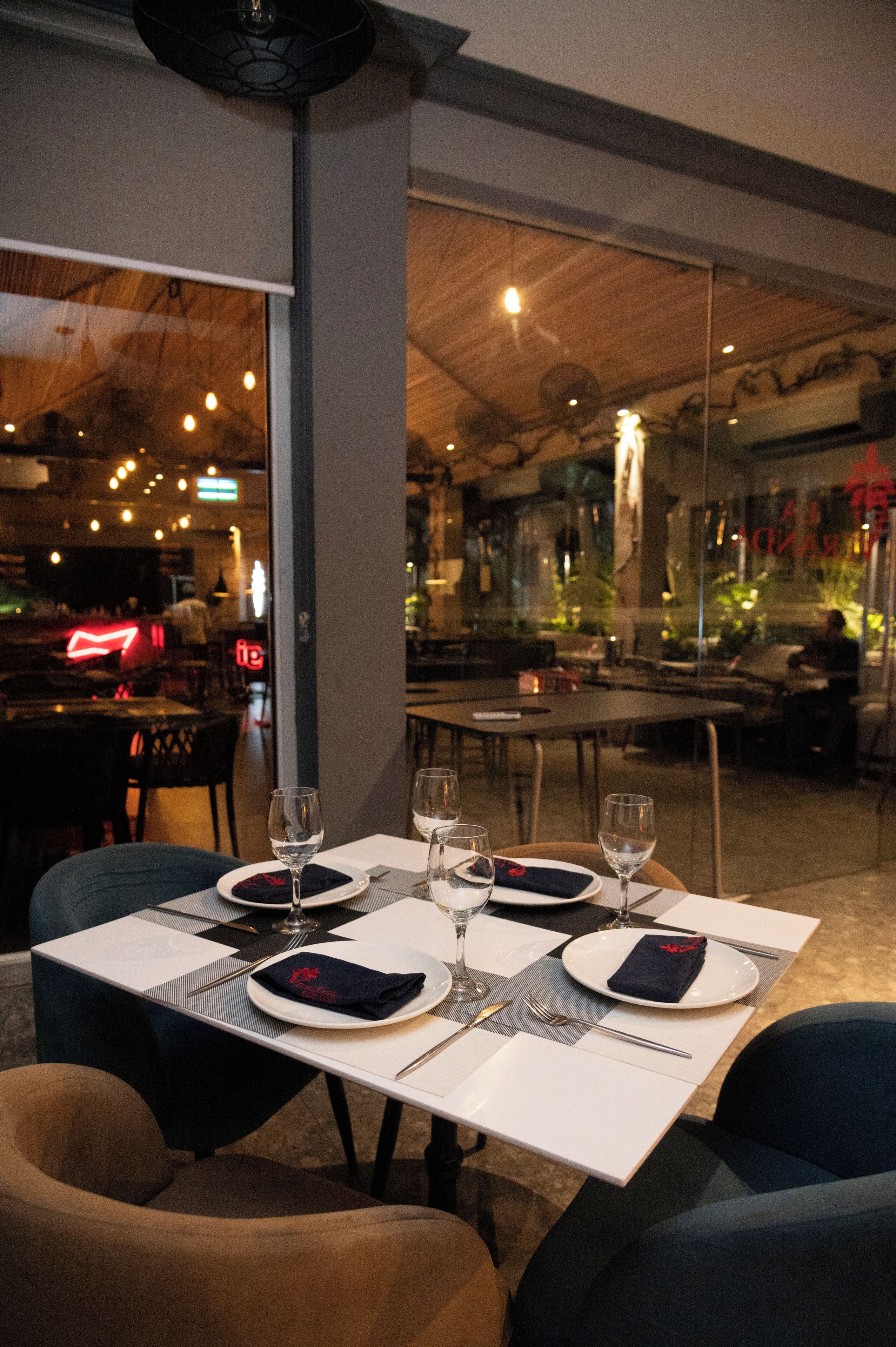 Comedor con mesas dispuestas para cuatro comensales, cada una con mantel blanco, platos, cubiertos y copas de vino.