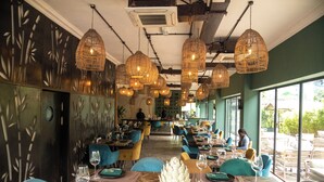 A restaurant with multiple dining tables, wicker hanging lights, and a view of the outdoors. - The Blowfish Hotel (Lagos)