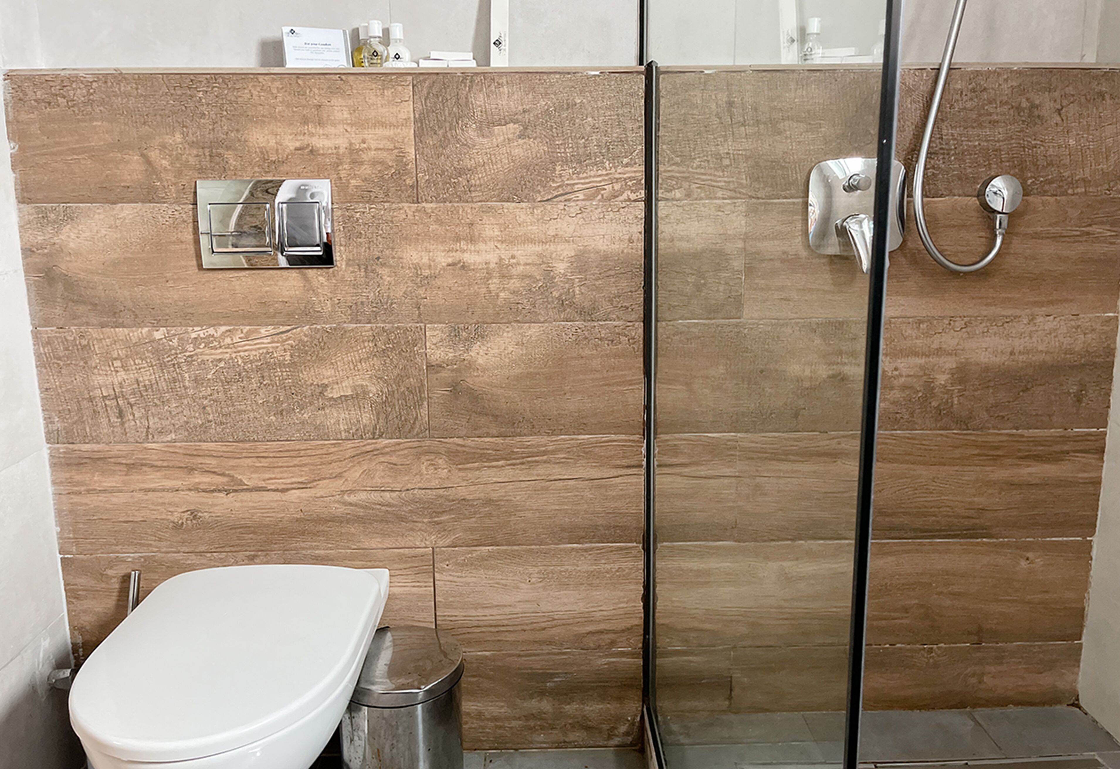 A bathroom with a wooden wall, a toilet, and a shower with a glass door.