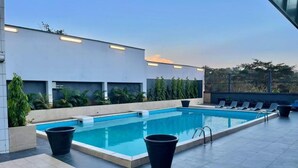 Une piscine sur le toit, avec une eau d’un bleu limpide, des poubelles noires et des chaises longues.
