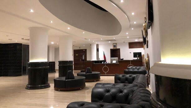 Un hall d'entrée moderne avec un comptoir d'accueil, des sièges en cuir noir et une grande colonne décorative.