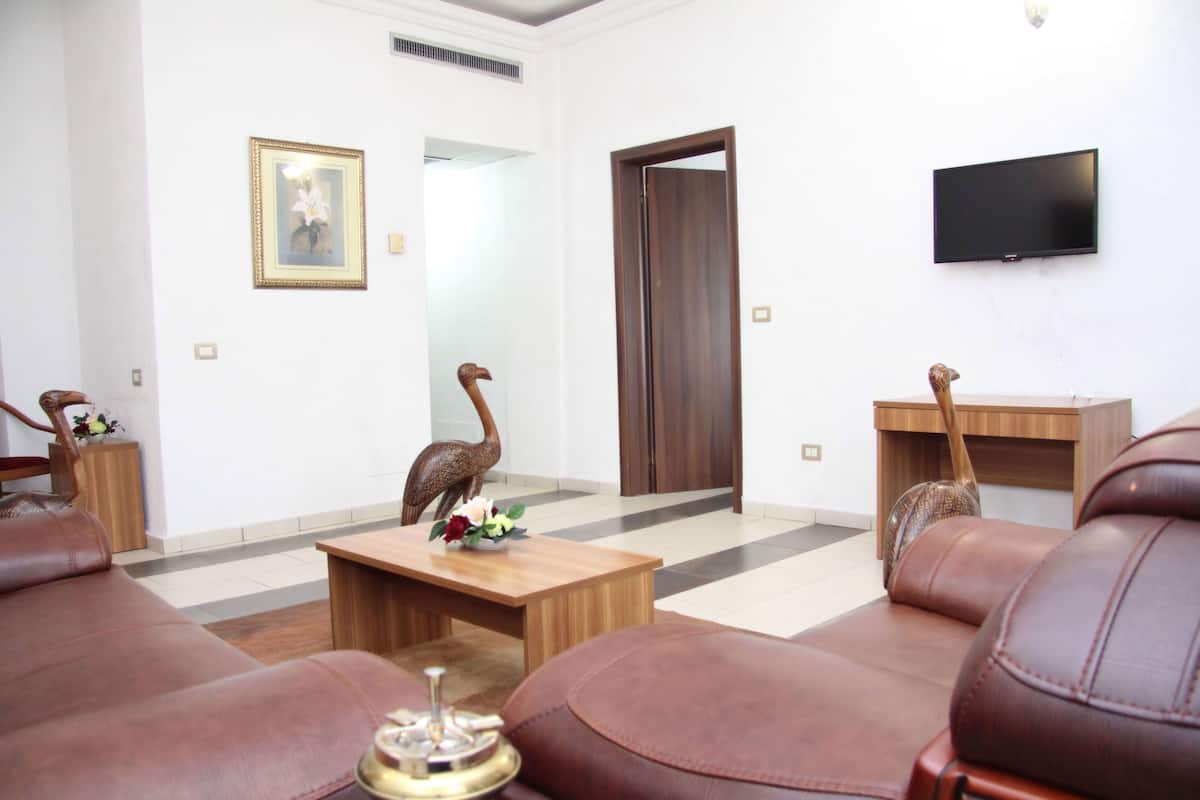 A modern living room with leather sofas, a wooden coffee table, a flat-screen TV, and decorative wooden sculptures.