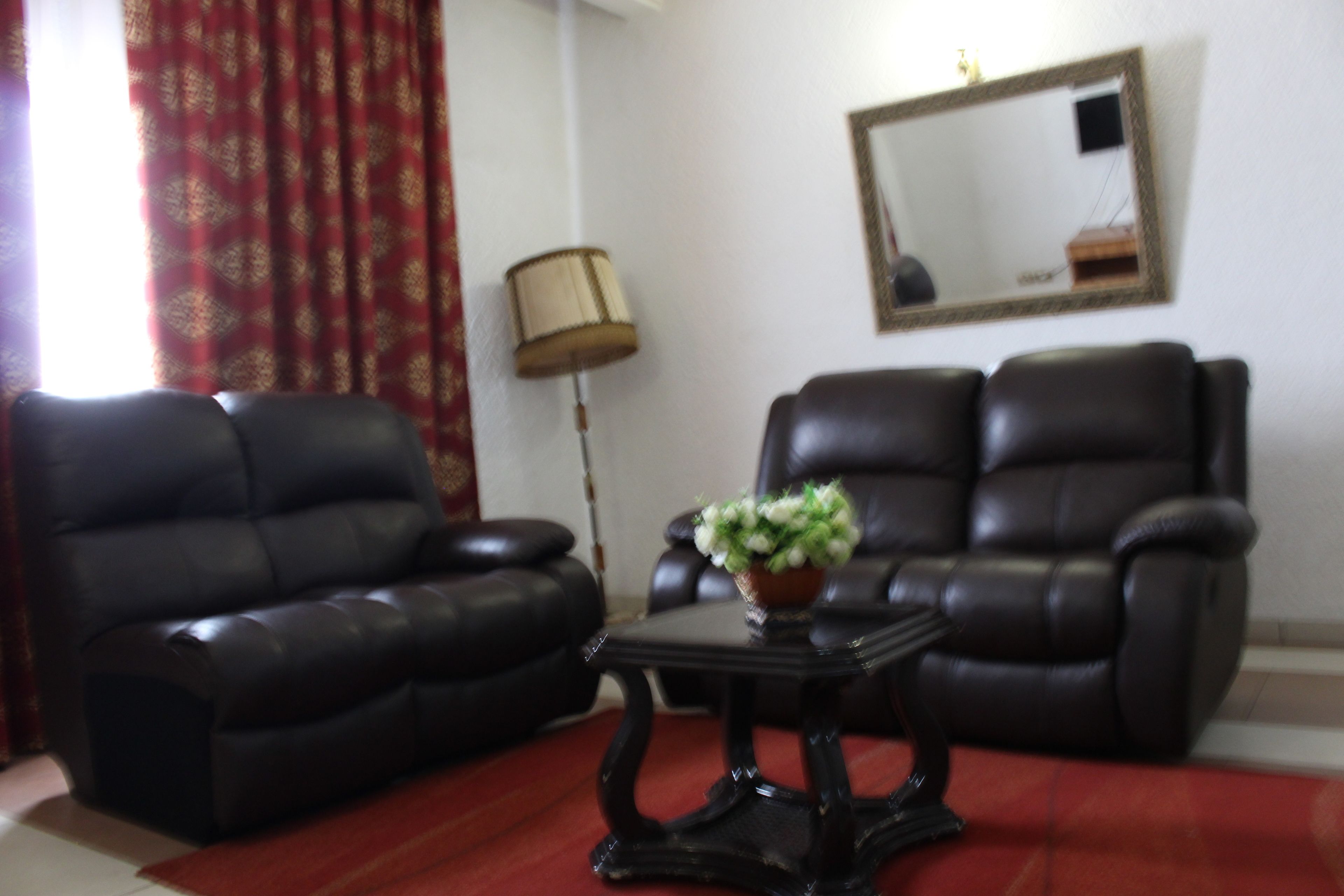 Una sala de estar con dos sofás de cuero negro, una mesita con un florero, una lámpara y un espejo en la pared.