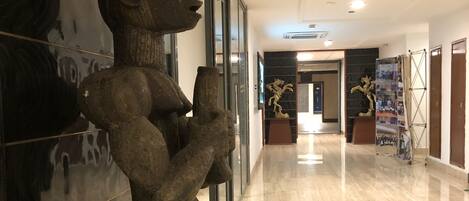 A hallway with a large abstract sculpture, a polished floor, and a framed photo display.