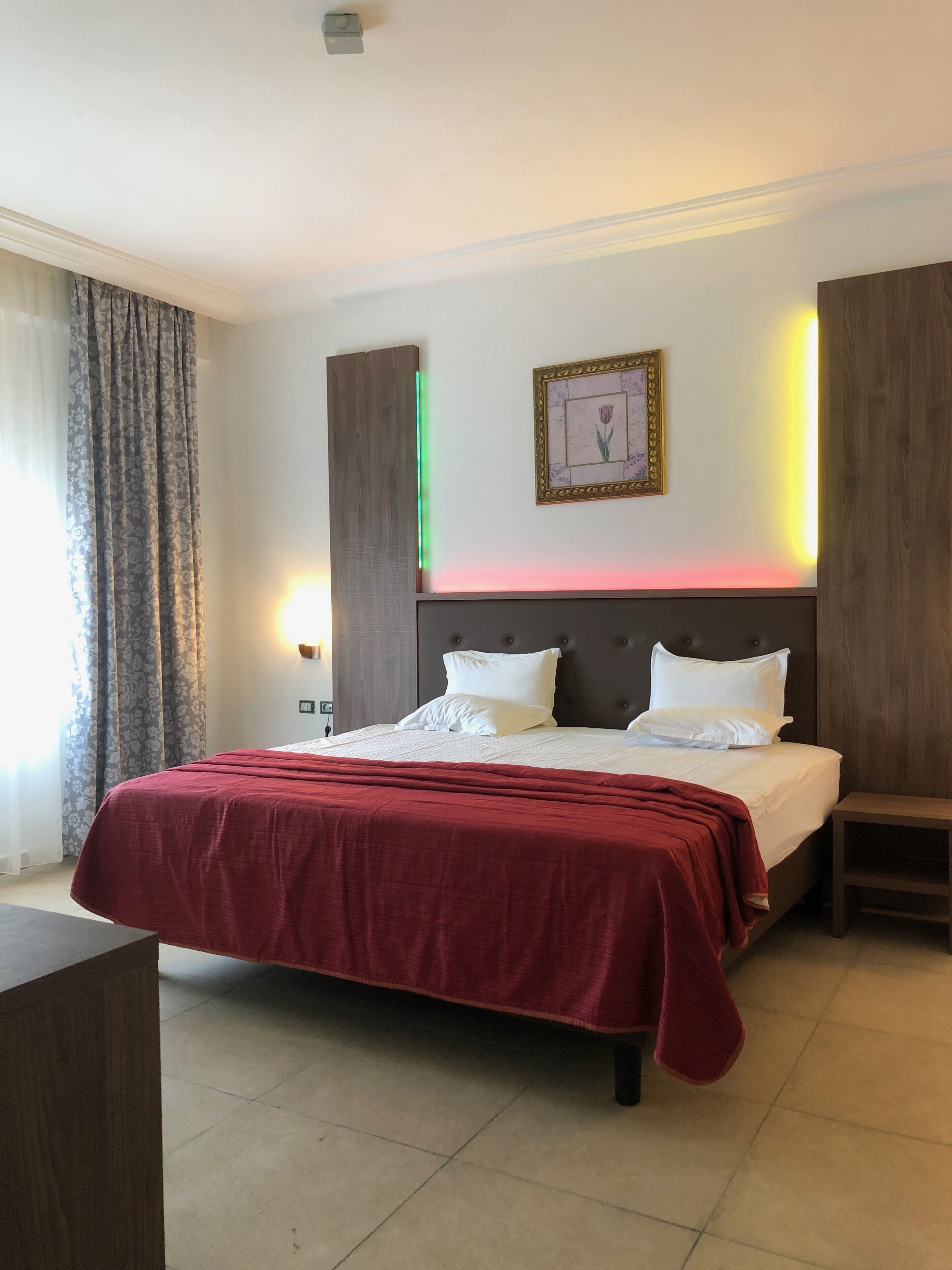 A hotel room with a large bed, a bedside table, a nightstand, and a wall-mounted picture frame.