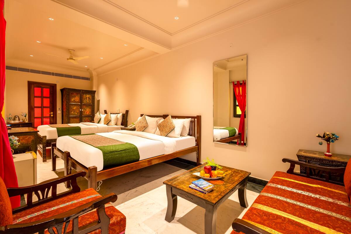 A hotel room with two beds, a wooden coffee table with fruit, a mirror, and a red curtain.