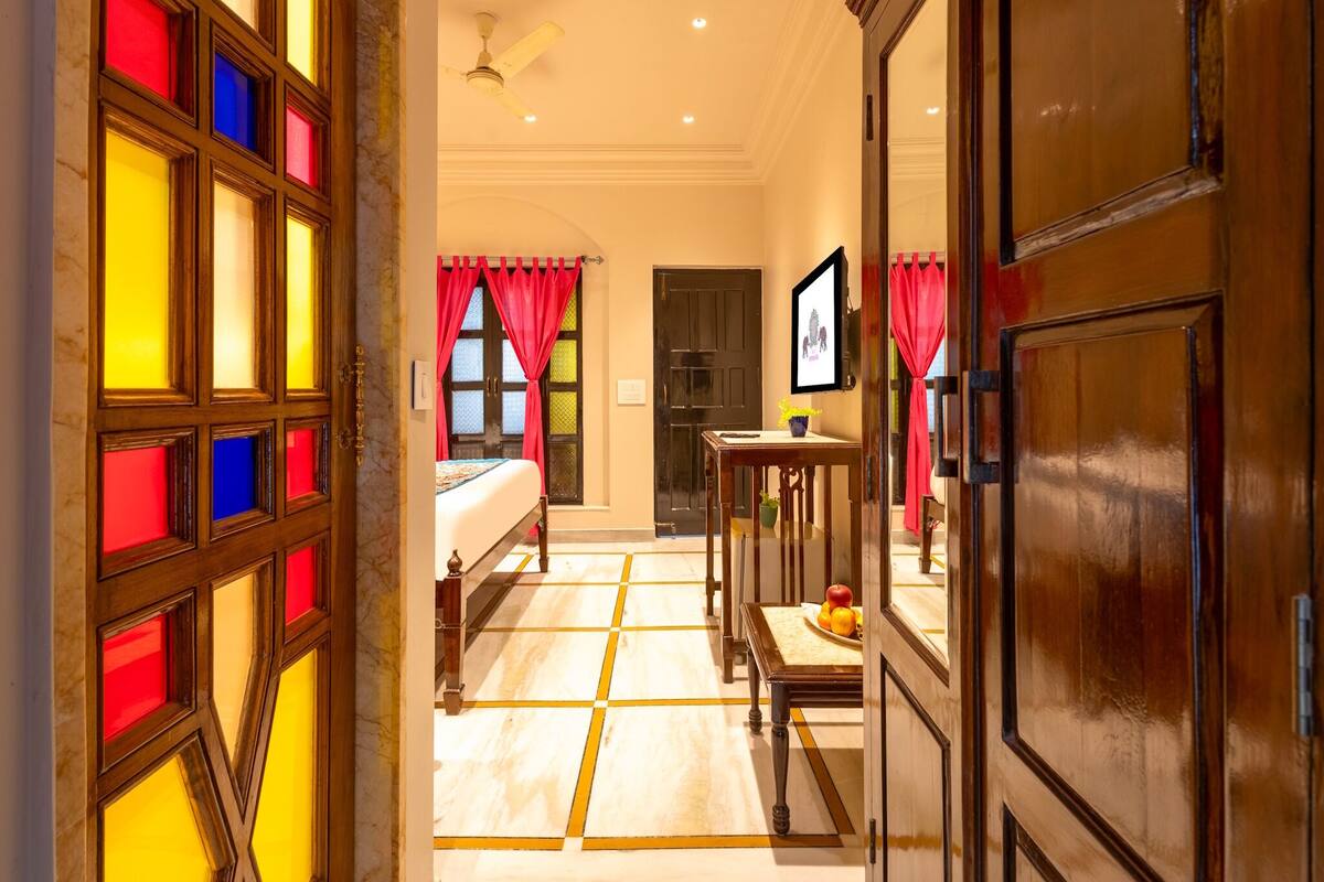 A hotel room with a bed, a desk, a chair, and a window with red curtains.