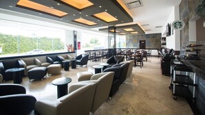 A spacious indoor area with multiple seating arrangements, including sofas and tables, and a kitchen area with a coffee machine. - Hotel Ankara Las Lomas (San Luis Potosi)