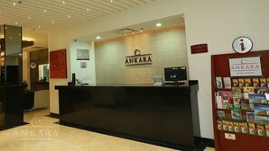 A hotel reception area with a modern design, featuring a reception desk, a wall-mounted sign, and a bulletin board with brochures. - Hotel Ankara Las Lomas (San Luis Potosi)