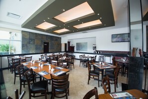 Un restaurant spacieux avec de hauts plafonds, un éclairage encastré et un mélange de chaises en bois et de chaises rembourrées.
