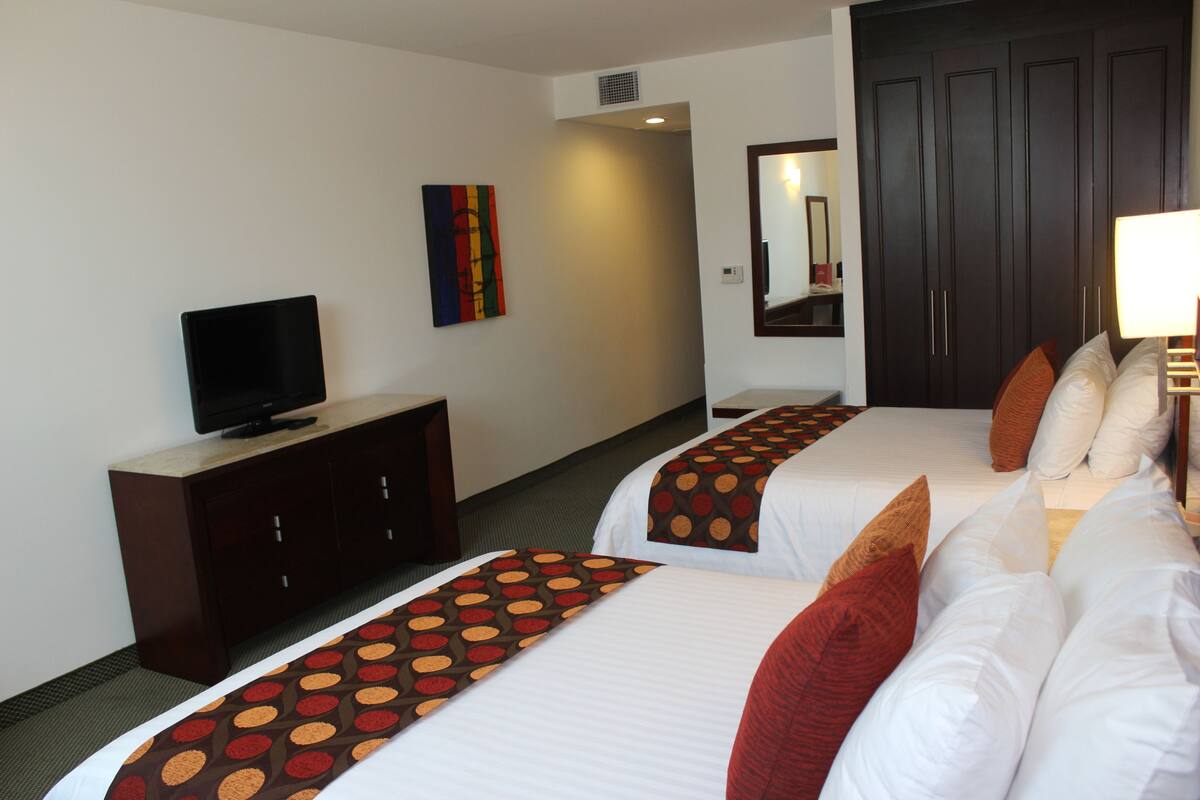 Una habitación de hotel con dos camas, un televisor en un mueble, un espejo y una puerta.